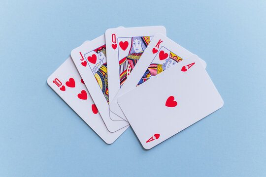 Royal flush hand of heart playing cards fanned out on a pastel light blue background. Minimalist flat lay stock photo representing luck, victory, casino games, and success.