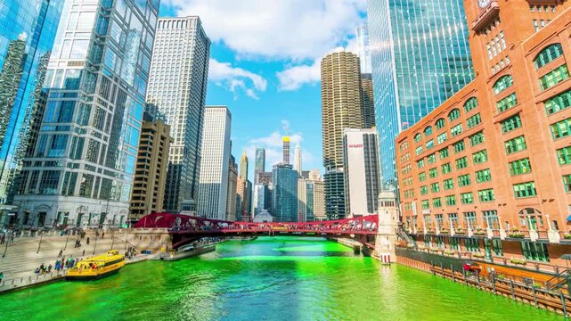 Chicago river dyed green for Saint Patrick Day celebration shows bright colorful water flowing under downtown bridges with skyscrapers and boat traffic scene.