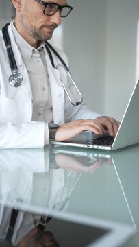 Doctor man working on laptop, entering patient information during online consultation in medical office. Medicine, healthcare and science concept