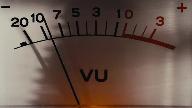 Mechanical measurement needle moving on scale of illuminated vintage VU meter display panel, indicating audio signal levels during playback. Macro shot