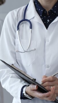 Medical professional writing on clipboard with stethoscope, a doctor and female assistant collaborating in a clinic, discussing patient data and healthcare information