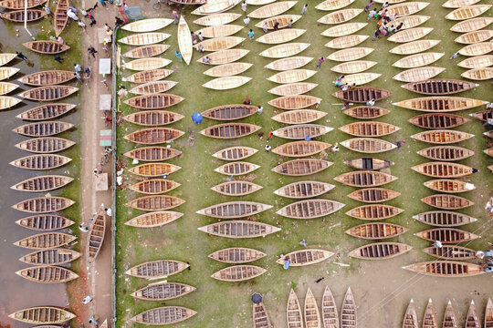 Manikganj, Bangladesh - 25 August 2021: Aerial view of Bost Market with numerous wooden boats lined up on the grassy riverbank and people walking nearby.