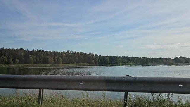 Calm lake with trees under a clear sky by a highway  