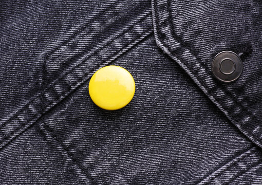 Yellow button badge pinned on gray jeans jacket