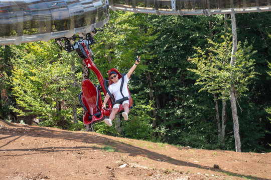 Tourist Riding a Suspended Mountain Coaster Above Forest with Scenic Lake and Mountain View, Summer Adventure Travel Attraction