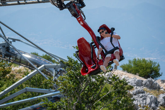 Tourist Riding a Suspended Mountain Coaster Above Forest with Scenic Lake and Mountain View, Summer Adventure Travel Attraction