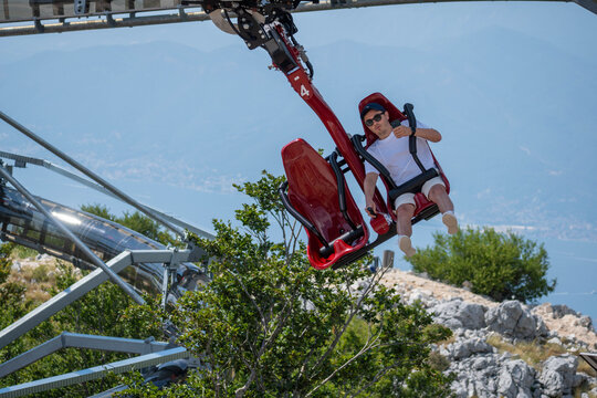 Tourist Riding a Suspended Mountain Coaster Above Forest with Scenic Lake and Mountain View, Summer Adventure Travel Attraction
