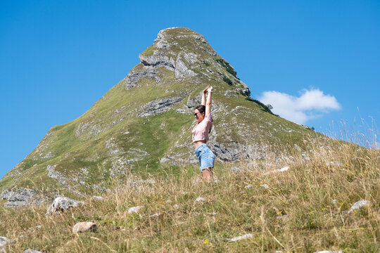 Young Woman Stretching with Arms Raised in Scenic Mountains, Outdoor Wellness, Freedom and Active Summer Travel Lifestyle