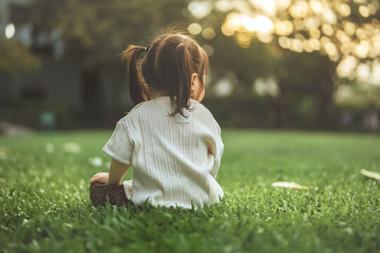 Young child sitting on green grass in park, peaceful outdoor childhood moment in nature at sunset