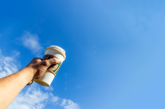 Hand Holding Coffee Cup Against Clear Blue Sky