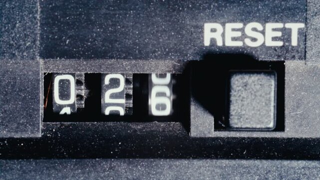 Three-digit mechanical analog counter displaying numbers on retro tape deck with reset button on side. Macro view