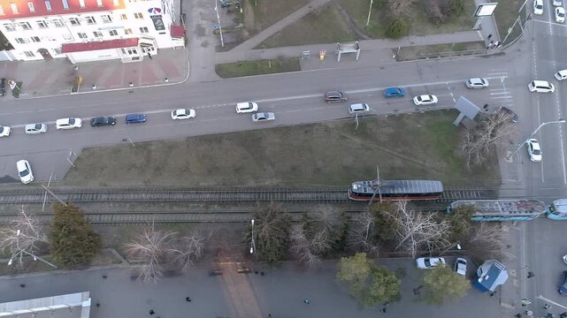 An aerial view of a tram moving through a city street in Krasnodar  Russia  surrounded by parked cars and greenery.