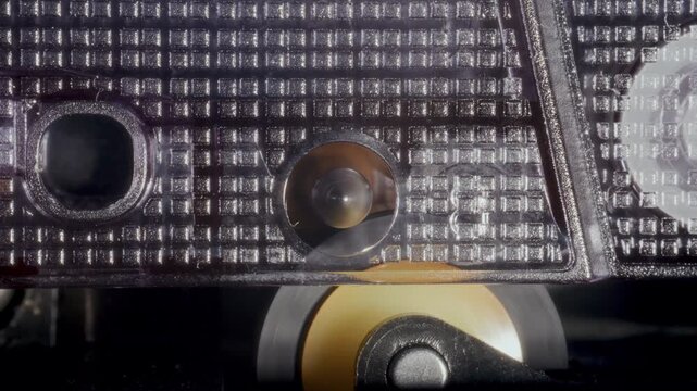 Metal capstan spindle and pinch roller rotating to pull magnetic tape ribbon of retro audio cassette tape. Detailed macro shot