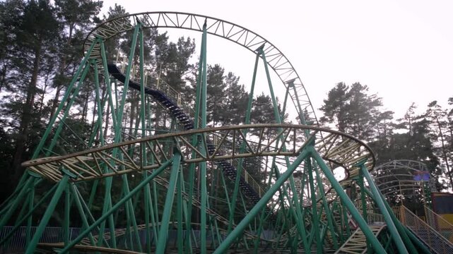 A wide shot of a green roller coaster track winding through a forested area  showcasing its intricate design and the surrounding natural environment.