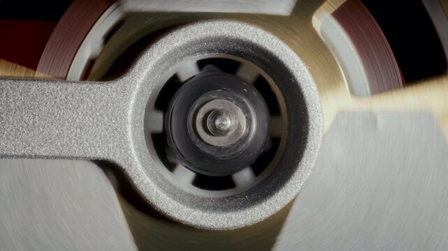 Detailed close-up view of central spindle hub and rotating magnetic tape ribbon of analog audio cassette tape spool during music playback