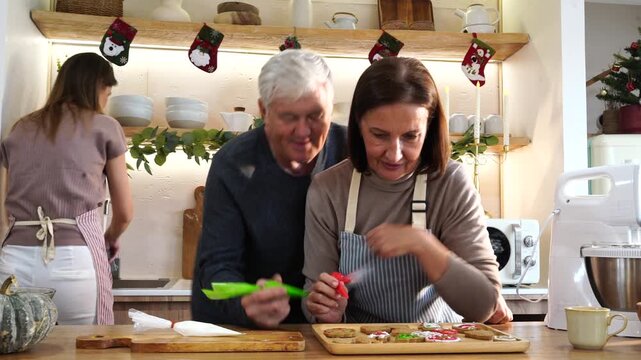 Grandpa and Grandma's family happily decorated gingerbread cookies together with cream cheese, preparing food for a Thanksgiving and Christmas party at home.

