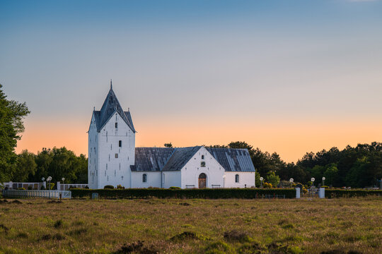 The historic white Romo Church, Romo Kirke, surrounded by a cemetery and green landscape under a beautiful sunset sky in Denmark.