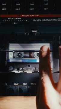 Hand loading audio cassette into retro multitrack recorder compartment, then pressing play button to turn on music. Vertical, close-up view