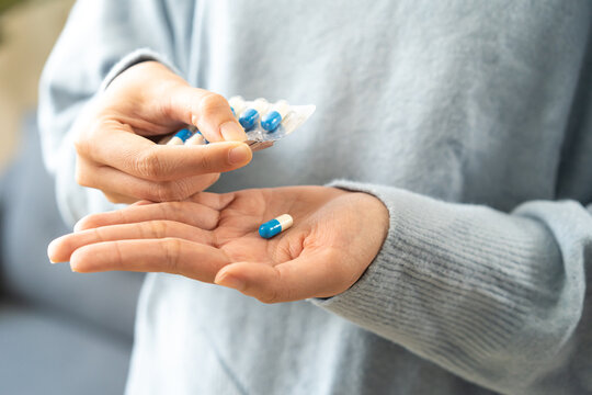 Sick asian young woman, girl taking tablet pill capsule out from blister pack, painkiller medicine for stomach pain, head ache, pain for treatment, take drug or vitamin at home, health care concept.
