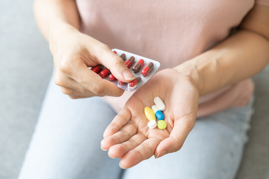 Sick ill asian young woman, girl hand taking tablet pill capsule out from blister pack, painkiller medicine from stomach pain, head ache, pain for treatment, take drug or vitamin at home, health care.