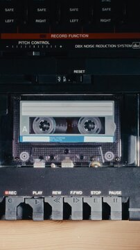 Retro analog multitrack studio recorder with compact audio cassette tape loaded inside deck compartment while playing music. Vertical, extreme close up shot