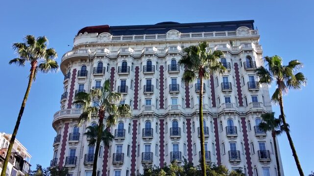 Elegant historic white building with balconies stands framed by tall palm trees against blue sky.