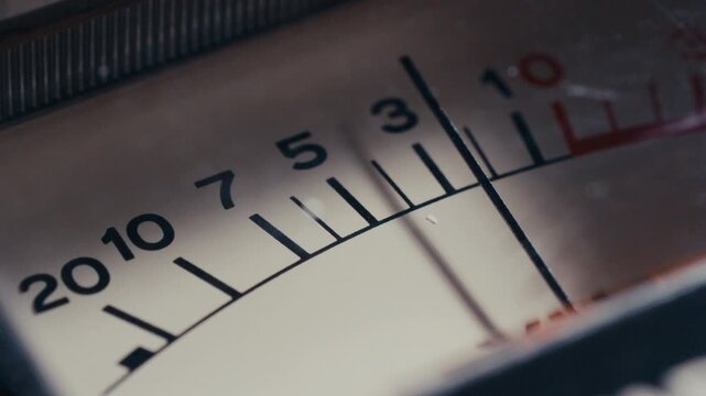 Mechanical indicator needle moving across numbered scale panel of retro analog VU meter. Extreme close-up shot