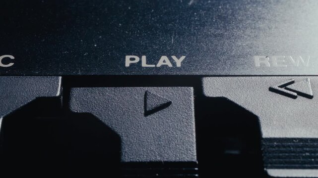 Finger pushing down plastic play button on retro cassette tape deck player, turning on music on analog audio device. Macro shot