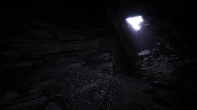 Bright portal light at cavern passage casting long shadows over rubble and slick stone, tense cinematic mood, directional contrast and texture detail
