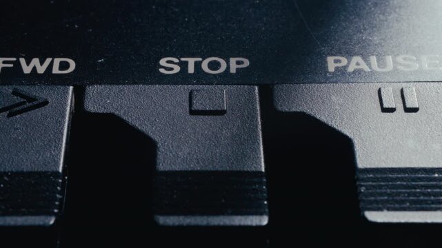 Finger pressing stop button on retro audio deck with STOP and PAUSE labels on black plastic control panel. Extreme close-up view