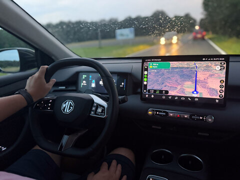 Driver's view inside a mg car on a rainy road, with hands on the wheel and a gps navigation screen glowing at dusk. MG S5 EV electric Poland, Pszczyna, 3.08.2026 
