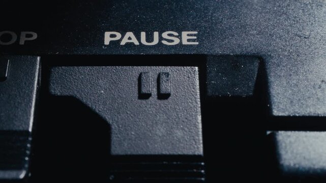 Finger pushing mechanical pause button on vintage cassette tape deck player, with word PAUSE written on plastic control panel. Macro shot
