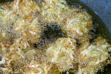 Fototapeta premium Vegetable fritters frying in hot oil in a wok. The main ingredients consist of sliced ​​cabbage, sliced ​​carrots, and sometimes bean sprouts