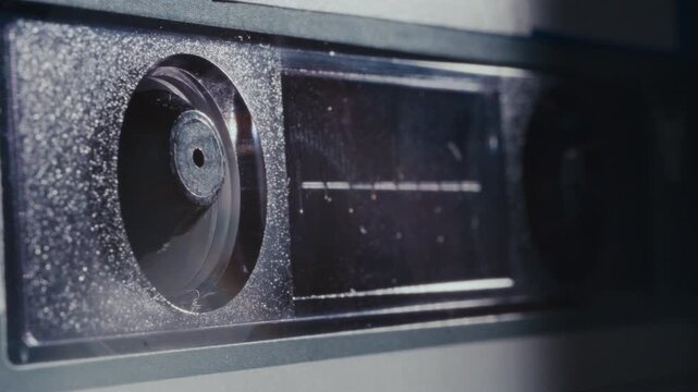 Dusty black compact audio cassette tape with internal spools spinning during analog music playback. Detailed macro shot