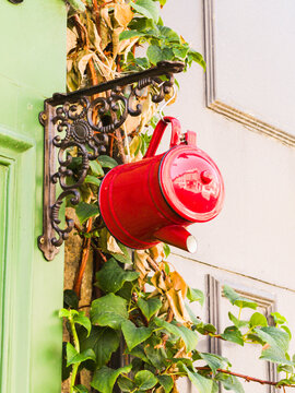 Decorative iron bracket holds a vintage red teapot on a wall. Ideal for garden decor advertisements, home renovation blogs, rustic style interiors.