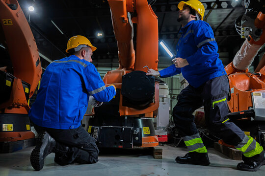 Two industrial engineers inspect a robotic arm during maintenance in a smart manufacturing facility, highlighting automation, engineering, teamwork, industrial robotics, and advanced production 