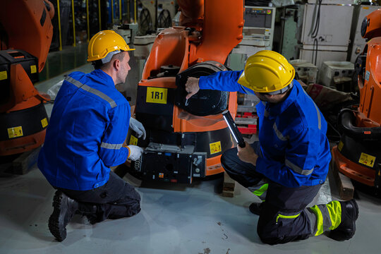 Two industrial engineers inspect a robotic arm during maintenance in a smart manufacturing facility, highlighting automation, engineering, teamwork, industrial robotics, and advanced production 