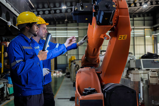Two industrial engineers inspect a robotic arm during maintenance in a smart manufacturing facility, highlighting automation, engineering, teamwork, industrial robotics, and advanced production 