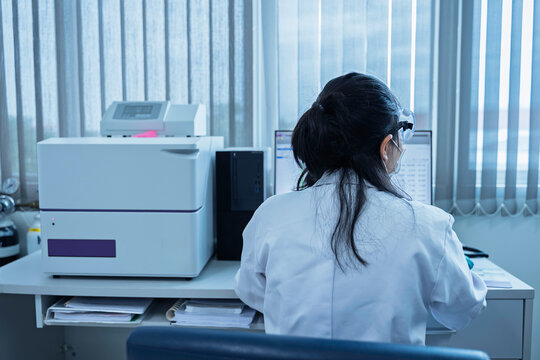 Female researcher analyzes experimental data on a computer beside a microplate reader in a laboratory. Concept of scientific research, biotechnology, diagnostics, and laboratory analysis.