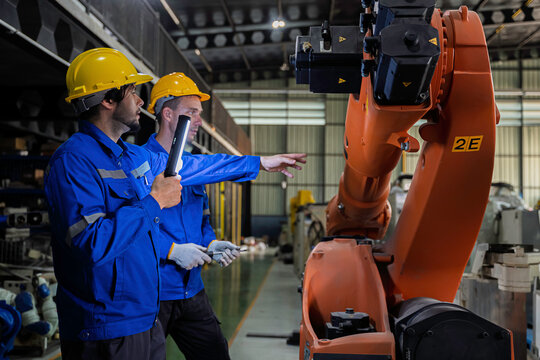 Two industrial engineers inspect a robotic arm during maintenance in a smart manufacturing facility, highlighting automation, engineering, teamwork, industrial robotics, and advanced production 