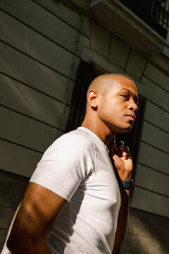 Black man in white t shirt posing in dramatic urban sunlight