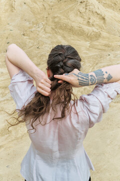 Girl braiding hair outdoors in a sandy location