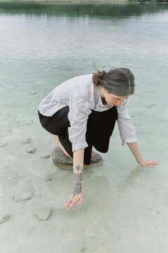 Young woman crouching near water and looking at stones