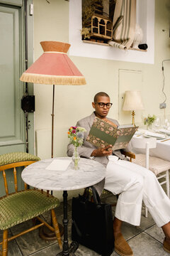 Man in tailored blazer reading menu at elegant outdoor cafe
