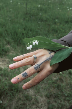 Girl holding a plant in nature with visible tattoos on her hand