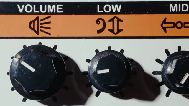 Finger turning three black knobs for volume, low bass and mid frequencies on retro guitar amplifier control panel. Macro shot