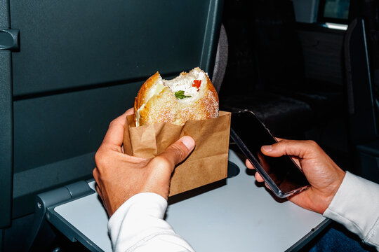 a man cradles a sandwich in a paper bag while checking his phone