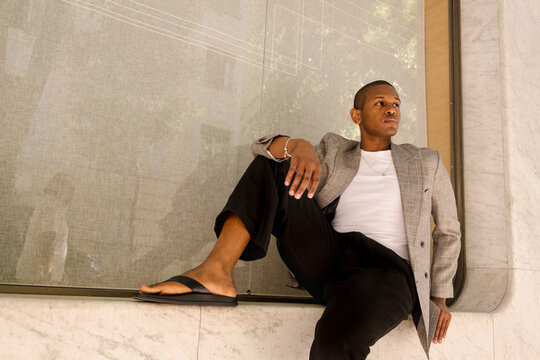 Man seated on marble ledge in street fashion editorial