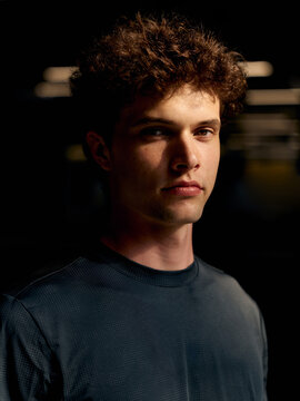 Young Man Stands in a Dark Setting With Focused Expression