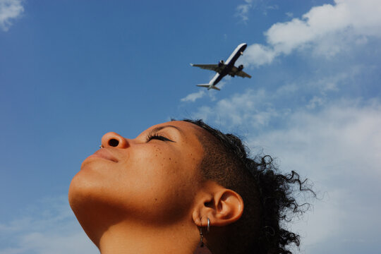 Woman looks up at airplane flying in the clear blue sky